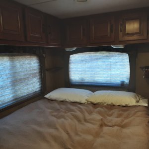 Queen bed with cabinets along side and back wall