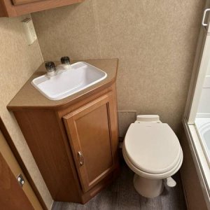 Small but functional bathroom. Porcelain Dometic foot-operated toilet. Corner sink and medicine cabinet. Shower has a skylight and a small, round vent