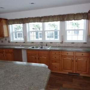 The kitchen.  In the foreground left, is a multi-level island with work/counter space on the lower side and a dining bar on the higher.