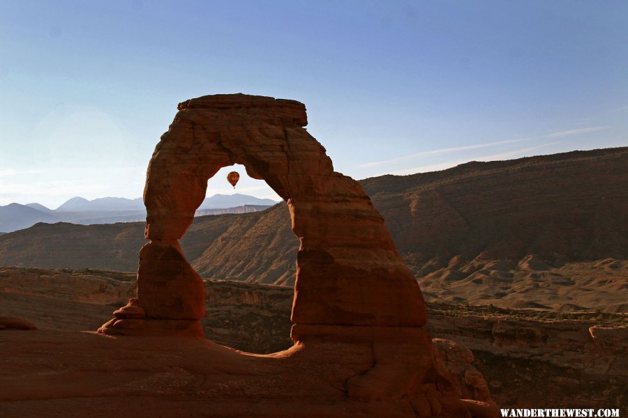 Delicate Arch with hot air balloon drifting by, seen through arch.